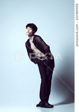 Full-length portrait of handsome, stylish, young guy posing in transparent black shirt against light blue studio background 102460409