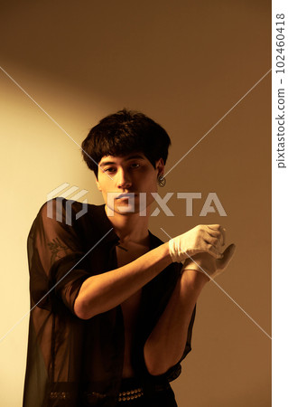 Elegant male look. Portrait of handsome young guy posing in transparent black shirt on naked relief body against studio background with sunlight 102460418