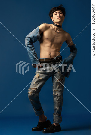 Portrait of young korean man posing shirtless in old style jeans against blue studio background. Weird fashion look 102460447