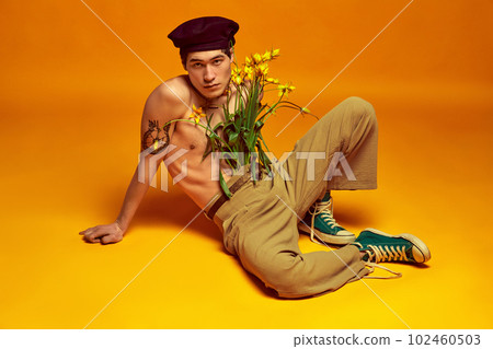 Youth vibe. Handsome, stylish, young korean guy posing shirtless with flowers, in beret and pants against yellow studio background Youth vibe. Handsome, stylish, young korean guy posing shirtless with flowers, in beret and pants against yellow studio background 102460503