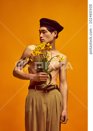 Parisian spring and summer collection. Handsome korean guy posing shirtless in classical pants, holding flowers against yellow studio background Parisian spring and summer collection. Handsome korean guy posing shirtless in classical pants, holding flowers against yellow studio background 102460508