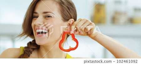 Happy young woman using slice of bell pepper as earring Happy young woman using slice of bell pepper as earring 102461092