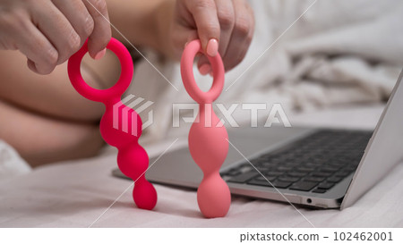 Woman holding a set of anal beads next to a laptop while lying in bed. Woman holding a set of anal beads next to a laptop while lying in bed. 102462001