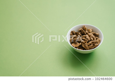 Peeled walnuts on a white plate on a green background with copy space Peeled walnuts on a white plate on a green background with copy space 102464600
