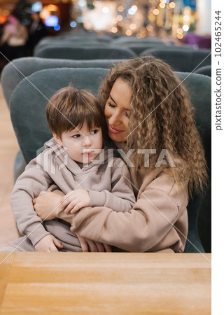 Little boy child is sitting on his mother's lap in a shopping and entertainment center in a food court cafe, a mother communicates with her son, spending time together 102465244