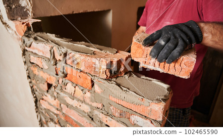 Close up of male hand in work glove laying brickwork in building under construction. Man builder placing brick on block course structure with cement mortar. Masonry construction concept. Close up of male hand in work glove laying brickwork in building under construction. Man builder placing brick on block course structure with cement mortar. Masonry construction concept. 102465590