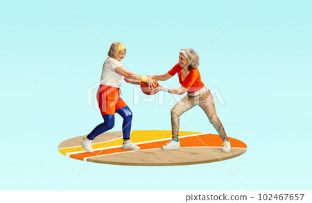 Competition. Two middle-aged, senior women in stylish sportswear playing with basketball ball against light blue background 102467657