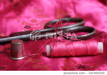 Spool of Pink Thread and Thimble on Vintage Pink Satin Fabric 102468300