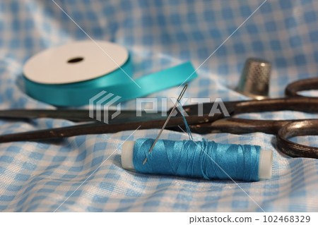 Spool of Blue Thread, Thimble and Needle on Blue and White Fabric 102468329