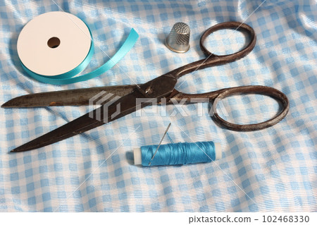 Spool of Blue Thread, Thimble and Needle on Blue and White Fabric Spool of Blue Thread, Thimble and Needle on Blue and White Fabric 102468330