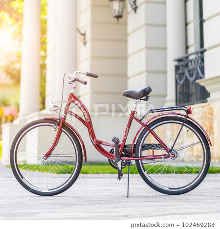 Bike at the summer sunset on the tiled road in the city park. Cycle closeup wheel on blurred summer background. Cycling down the street to work at summer sunset. Bicycle and ecology lifestyle concept. Bike at the summer sunset on the tiled road in the city park. Cycle closeup wheel on blurred summer background. Cycling down the street to work at summer sunset. Bicycle and ecology lifestyle concept. 102469283