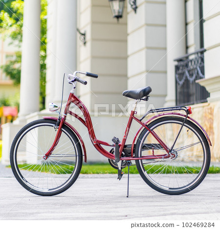 Bike at the summer sunset on the tiled road in the city park. Cycle closeup wheel on blurred summer background. Cycling down the street to work at summer sunset. Bicycle and ecology lifestyle concept. Bike at the summer sunset on the tiled road in the city park. Cycle closeup wheel on blurred summer background. Cycling down the street to work at summer sunset. Bicycle and ecology lifestyle concept. 102469284