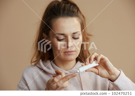 woman applying ointment using finger against beige background woman applying ointment using finger against beige background 102470251