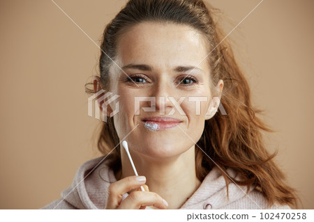 female applying ointment using cotton swab on beige background 102470258