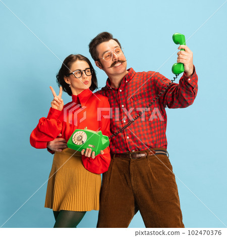 Portrait with stunning couple, man and woman holding telephone and smiling over blue studio background. Vintage style love story 102470376