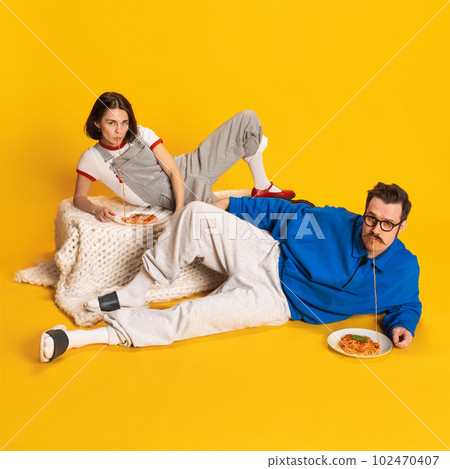 Portrait with charming couple handsome man and beautiful woman wearing stylish vintage clothes eating spaghetti together over yellow background 102470407
