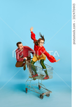 Portrait with funny couple, handsome man and excited woman riding in shopping cart over blue studio background. Black Friday sales Portrait with funny couple, handsome man and excited woman riding in shopping cart over blue studio background. Black Friday sales 102470443