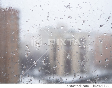 wet snow flakes on window glass in city apartment 102471129