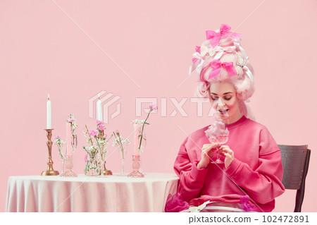 Portrait with fairy tail young princess wearing big pink wig holding wine glass with exciting face over pink studio background Portrait with fairy tail young princess wearing big pink wig holding wine glass with exciting face over pink studio background 102472891