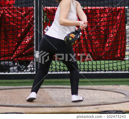 Female high school track athlete in the circle throwing a wieght during a weight throw competition Female high school track athlete in the circle throwing a wieght during a weight throw competition 102473243