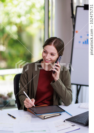 Concept of business office woman working,Businesswoman smile while working about her invesment plan with analyzing document and business investment graph data by using laptop on desk in workstation. 102475731