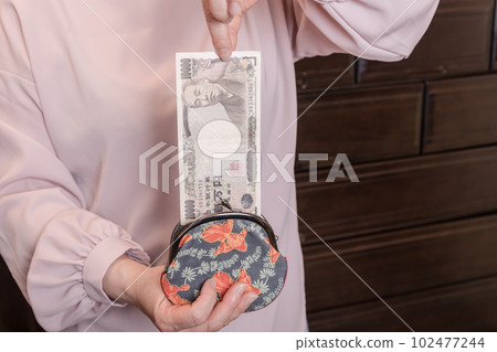 [一位家庭主婦從釦子裡拿出一張 10,000 日元的鈔票] 102477244