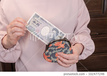 [一位家庭主婦從釦子裡拿出一張 1000 日元的鈔票] 102477246