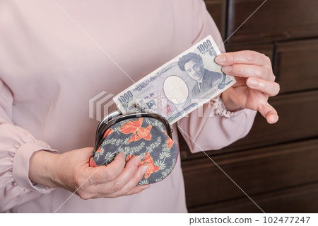 [一位家庭主婦從釦子裡拿出一張 1000 日元的鈔票] 102477247