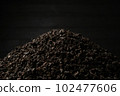 A pile of black fanning or broken loose leaf tea on a dark black background. Close-up, side view. 102477606