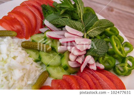 Plate of fresh vegetable salad, tomato, cucumber, onion, gherkin, radish, mint leaves on turntable 102477631