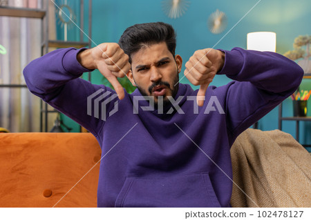 Upset indian man showing thumbs down, dislike bad work, disapproval, dissatisfied feedback at home 102478127