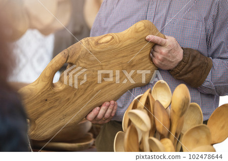 Production of wooden products in the concept of small business. Carpenter holding a rare wood tray in a carpentry workshop. Manufacture and sale of wooden furniture. 102478644