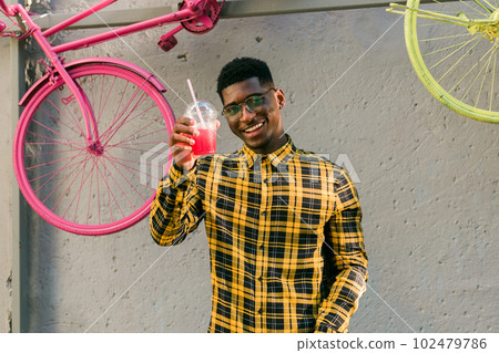 Young cheerful african american male on city having fun and holding cocktail. Man on summer holiday. Leisure lifestyle holiday and summer drinks concept Young cheerful african american male on city having fun and holding cocktail. Man on summer holiday. Leisure lifestyle holiday and summer drinks concept 102479786