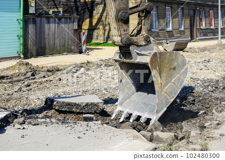 Closeup of a hydraulic excavator bucket breaking up the asphalt layer before street reconstruction Closeup of a hydraulic excavator bucket breaking up the asphalt layer before street reconstruction 102480300