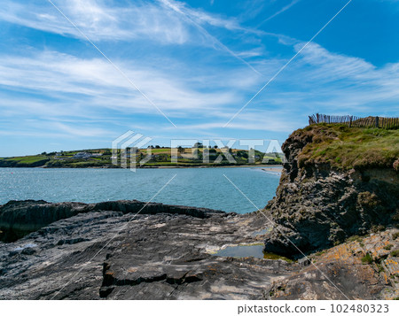 A sheer stone cliff on the Atlantic Ocean in Ireland on a sunny summer day. Irish seaside landscape, clear blue sky, rock formation near body of water. A sheer stone cliff on the Atlantic Ocean in Ireland on a sunny summer day. Irish seaside landscape, clear blue sky, rock formation near body of water. 102480323
