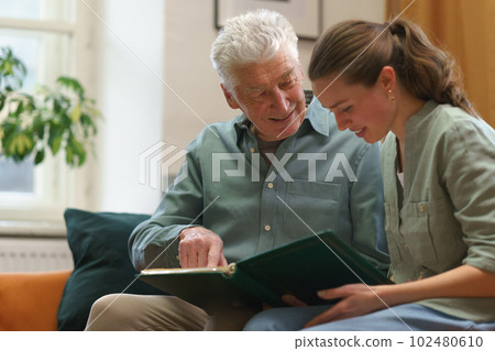 Senior man with his grandaughter looking family photo album. 102480610