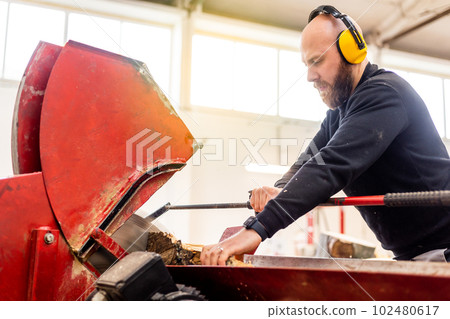 Professional carpenter cutting raw wood to firewood pieces, manufacturing wood concept Professional carpenter cutting raw wood to firewood pieces, manufacturing wood concept 102480617