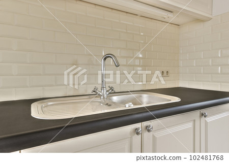 a kitchen with white tiles on the wall and black countertop in front of the sink is visible to the right a kitchen with white tiles on the wall and black countertop in front of the sink is visible to the right 102481768