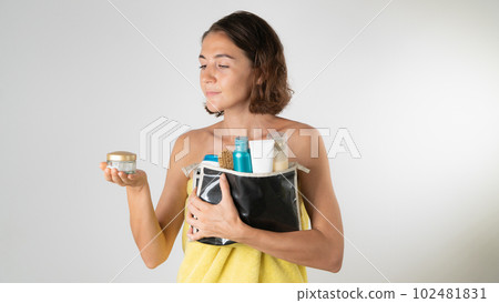 A woman with a cosmetic bag and face cream in her hands after a shower - a procedure for self-care at home 102481831