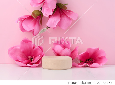 Empty round wooden platform and branches with pink magnolia flowers on a pink background. Place for demonstration of products 102484968