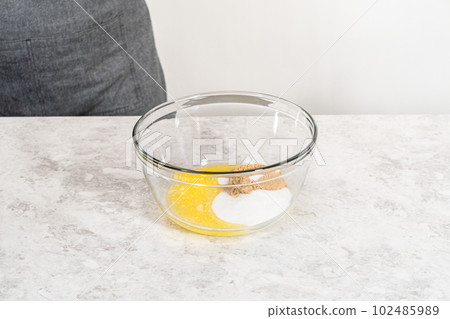 Mixing wet and dry ingredients with a hand whisk in a glass mixing bowl to bake a carrot bundt cake with cream cheese frosting. 102485989