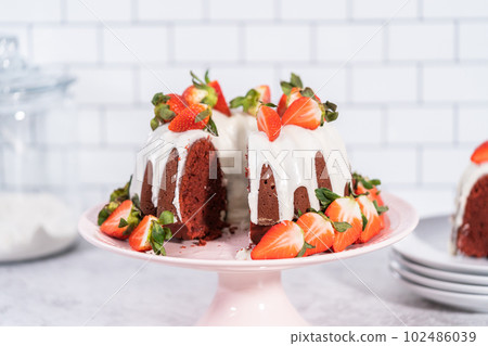 Slicing red velvet bundt cake with cream cheese frosting garnished with fresh strawberries. Slicing red velvet bundt cake with cream cheese frosting garnished with fresh strawberries. 102486039