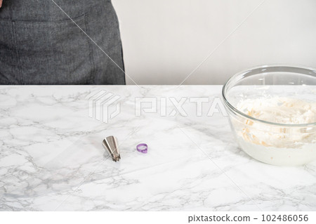 Whisking buttercream frosting in a glass mixing bowl with an electric hand mixer to prepare the peppermint buttercream frosting. 102486056
