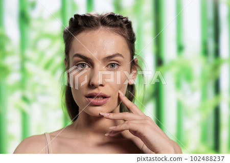 Young caucasian skincare model posing with fingers on face portrait. Natural beautiful woman showing glowing skin after organic cosmetology treatment on bamboo background Young caucasian skincare model posing with fingers on face portrait. Natural beautiful woman showing glowing skin after organic cosmetology treatment on bamboo background 102488237