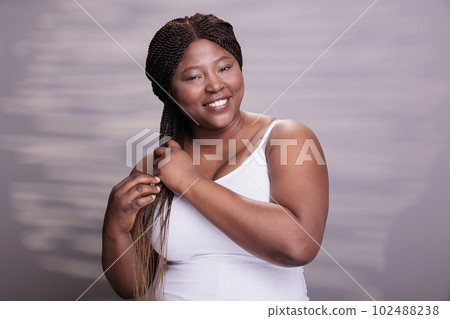 African american woman showing hair braiding technique, making african hairstyle tutorial. Natural beautiful plus size model smiling, looking at camera with carefree facial expression African american woman showing hair braiding technique, making african hairstyle tutorial. Natural beautiful plus size model smiling, looking at camera with carefree facial expression 102488238