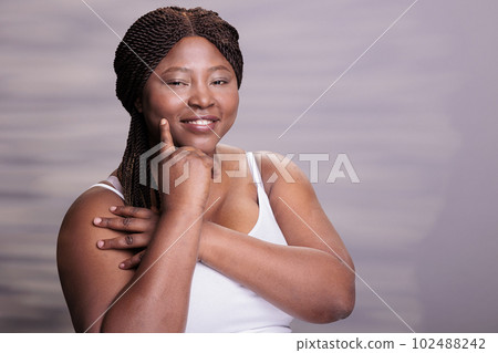 Natural beautiful skincare body positive model touching cheek portrait. African american curvy woman pointing on perfect healthy skin, holding finger on face and looking at camera Natural beautiful skincare body positive model touching cheek portrait. African american curvy woman pointing on perfect healthy skin, holding finger on face and looking at camera 102488242