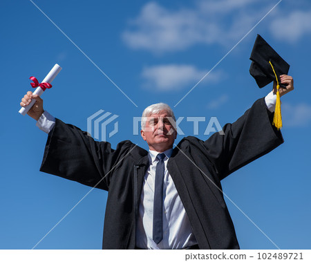 Elderly male graduate rejoices in receiving a diploma against a blue sky. Elderly male graduate rejoices in receiving a diploma against a blue sky. 102489721