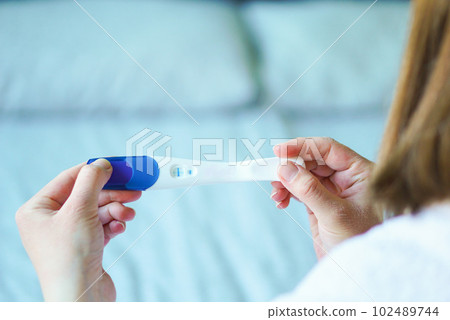 Women holding a baby pregnancy test with two stripes. Positive result. 102489744
