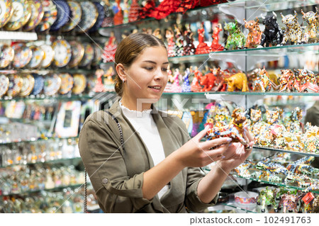Cheerful female tourist choosing colorful bull statuette at tourist shop 102491763