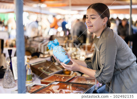 Happy female tourist looking to buy pretty ceramic vase at flea market Happy female tourist looking to buy pretty ceramic vase at flea market 102492135